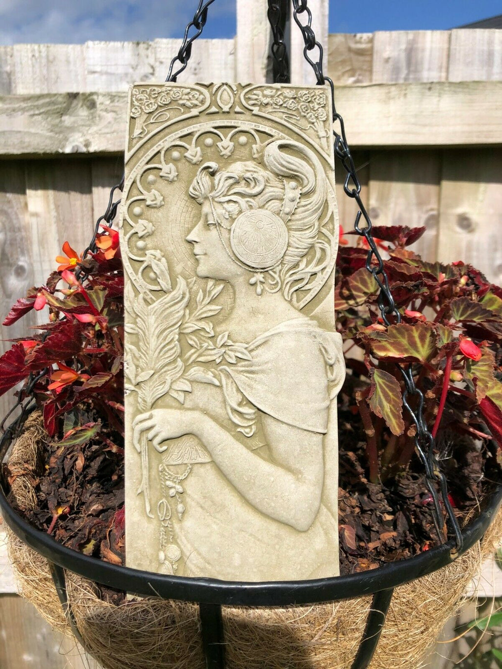 A female fairy standing in profile with a halo of leaves on a rectangular plaque. Situated in the flowerbed of a British garden