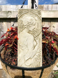 A profile of a lady on a rectangular plaque with a halo of flowers. Situated in the flowerbed of a British Garden
