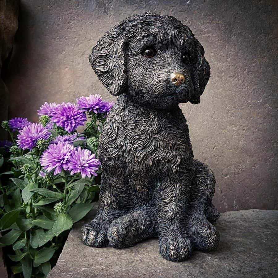 A fluffy puppy of bronze finish with floppy ears and detailed fur. Sitting on the stone table of a British home with purple flowers in the background