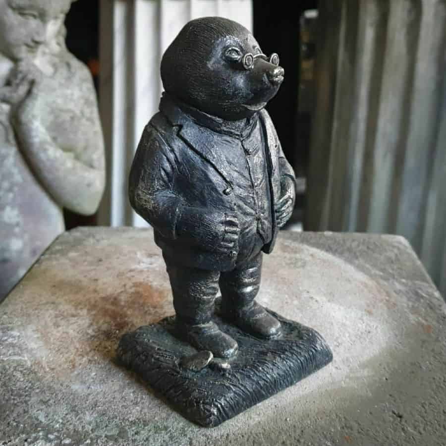 Mole from Wind in the Willows featuring spectacles and waiste-jacket. Sitting on a marble plinth in a British statue store
