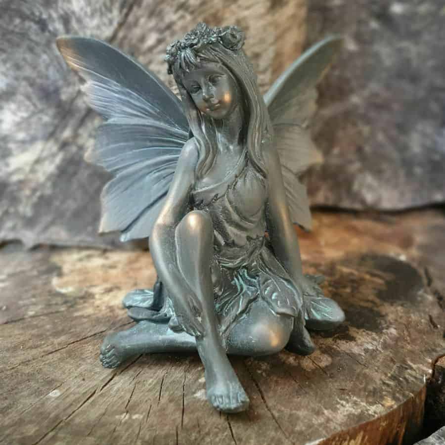 An graceful fairy with crown of leaves and flowing dress. Sitting on the log of a British garden