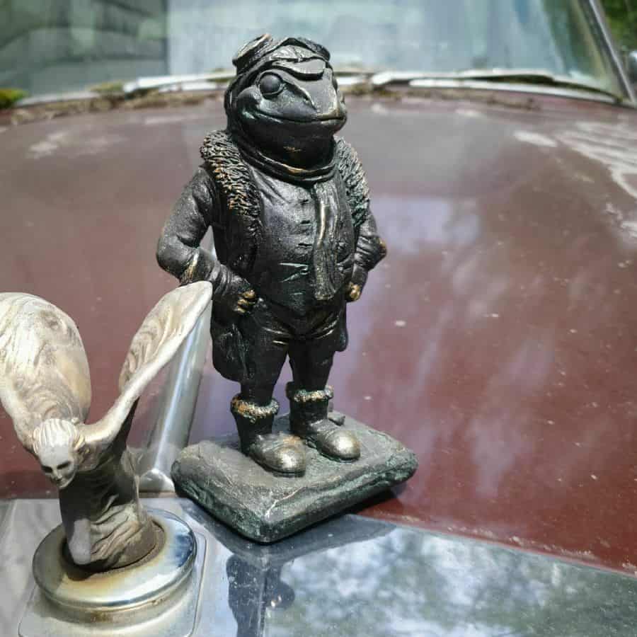 Mr. Toad from The Wind in the Willows. A toad adorned with driving spectacles and jacket. Situated on the hood of a vintage car