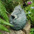 A hedgehog curled up into a ball of grey finish. Situated on a wooden log amongst the foliage of a British garden