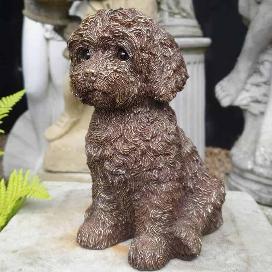 A puppy dog sitting with a loving look, fluffy coat and large ears. Sitting amongst other statues in a British garden