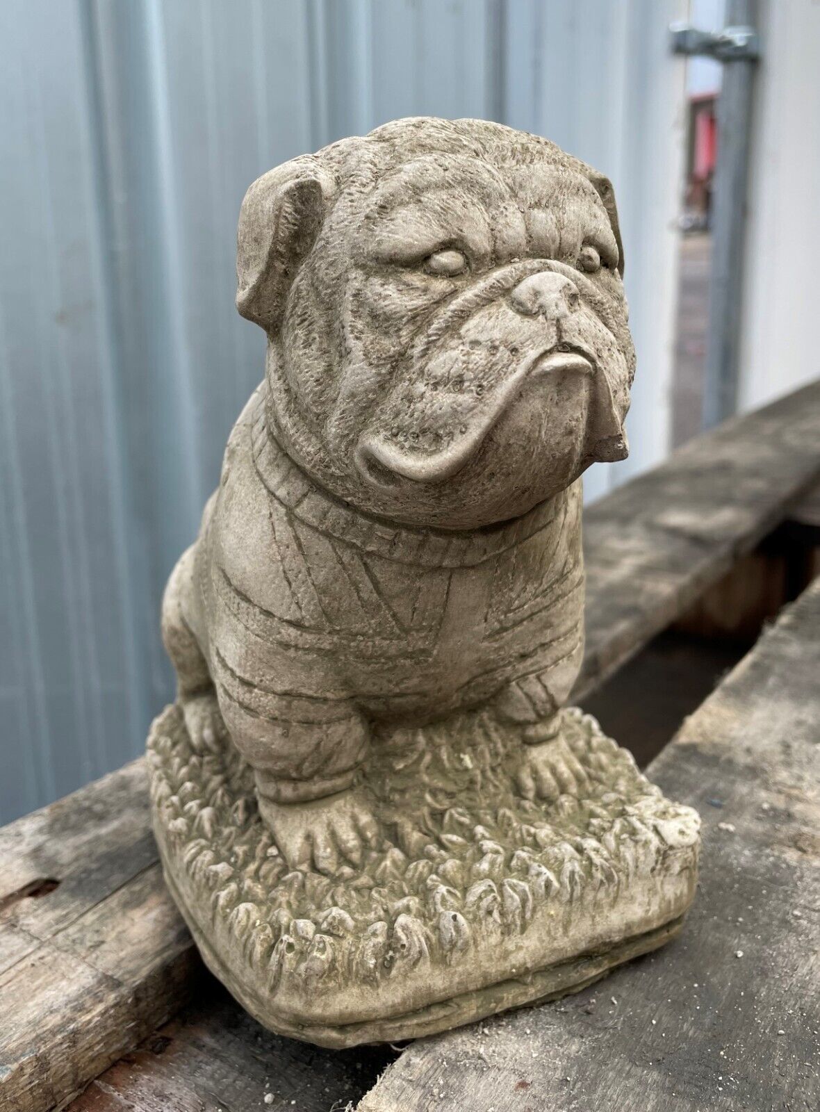 A British Bulldog Stone statue sporting a Union Jack jumper - sitting on the grass.