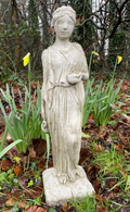 A lady with flowing robes and tied back hair, standing amongst the sprouting yellow daffodils in a British garden