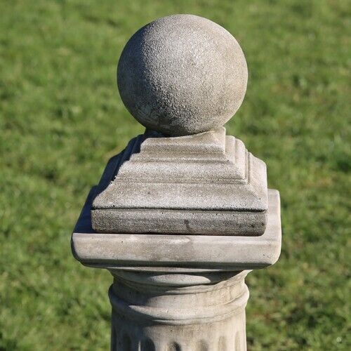 A spherical finial with base. Situated on a plinth in a British garden with green grass in the background