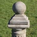 A spherical finial with base. Situated on a plinth in a British garden with green grass in the background