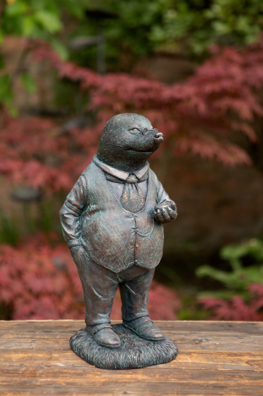A Mr Mole figure with waistcoat and timepiece. Situated in the garden of a British home with red foliage in the background
