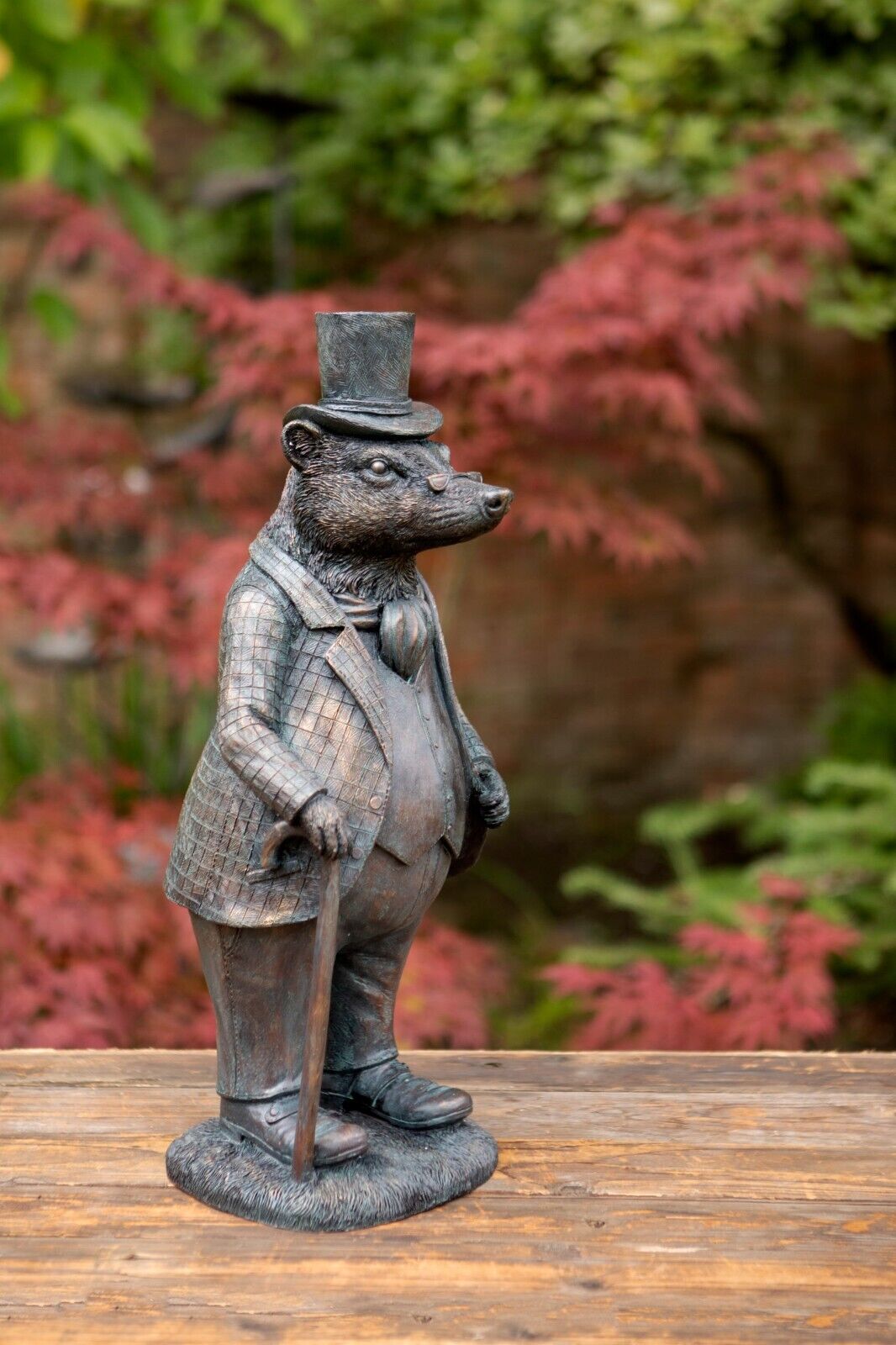 A Mr Badger figure adorned with cane and top hat. Situated in a British garden with red foliage in the background