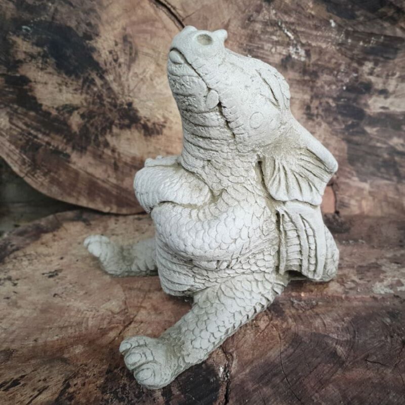A stubby dragon with arms folded and a pouting expression, sitting on a log in a British garden