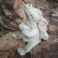 A stubby dragon with arms folded and a pouting expression, sitting on a log in a British garden