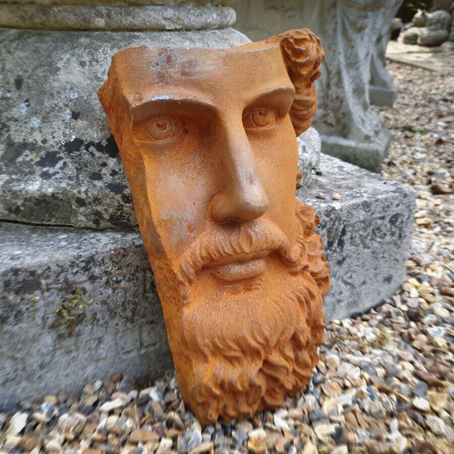 The face of a bearded roman man in rusted iron finish. Situated on the gravel of a British garden