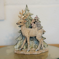 A reindeer of brown colour with woodland critters on back walking amongst the Christmas trees. Situated on the dinner table of a British home