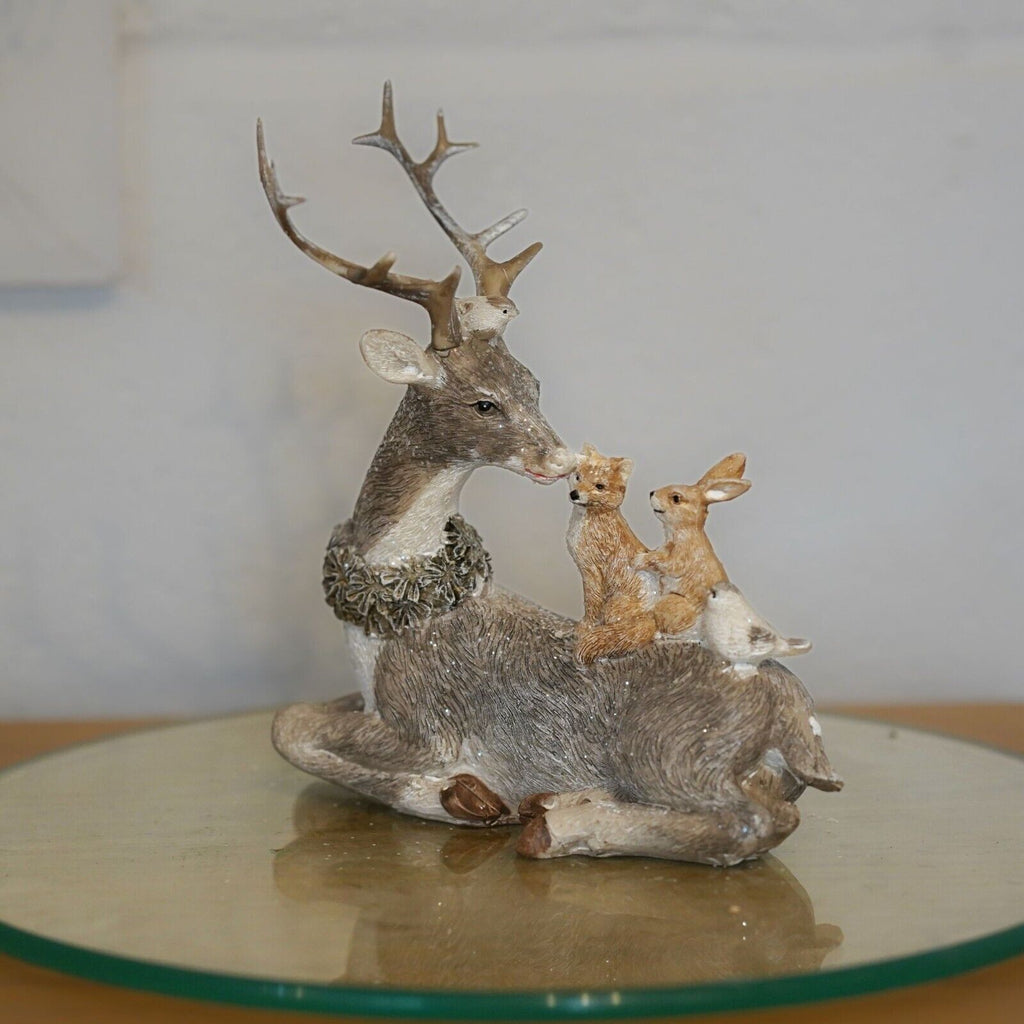 A grey reindeer with antlers and wreath around neck, laying with forest critters on back. Situated on a glass plinth in a British home
