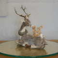 A grey reindeer with antlers and wreath around neck, laying with forest critters on back. Situated on a glass plinth in a British home