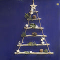 Wooden twigs assembled to resemble a christmas tree, attached with strings and adorned with pinecones and forest leaves with a wooden star on top