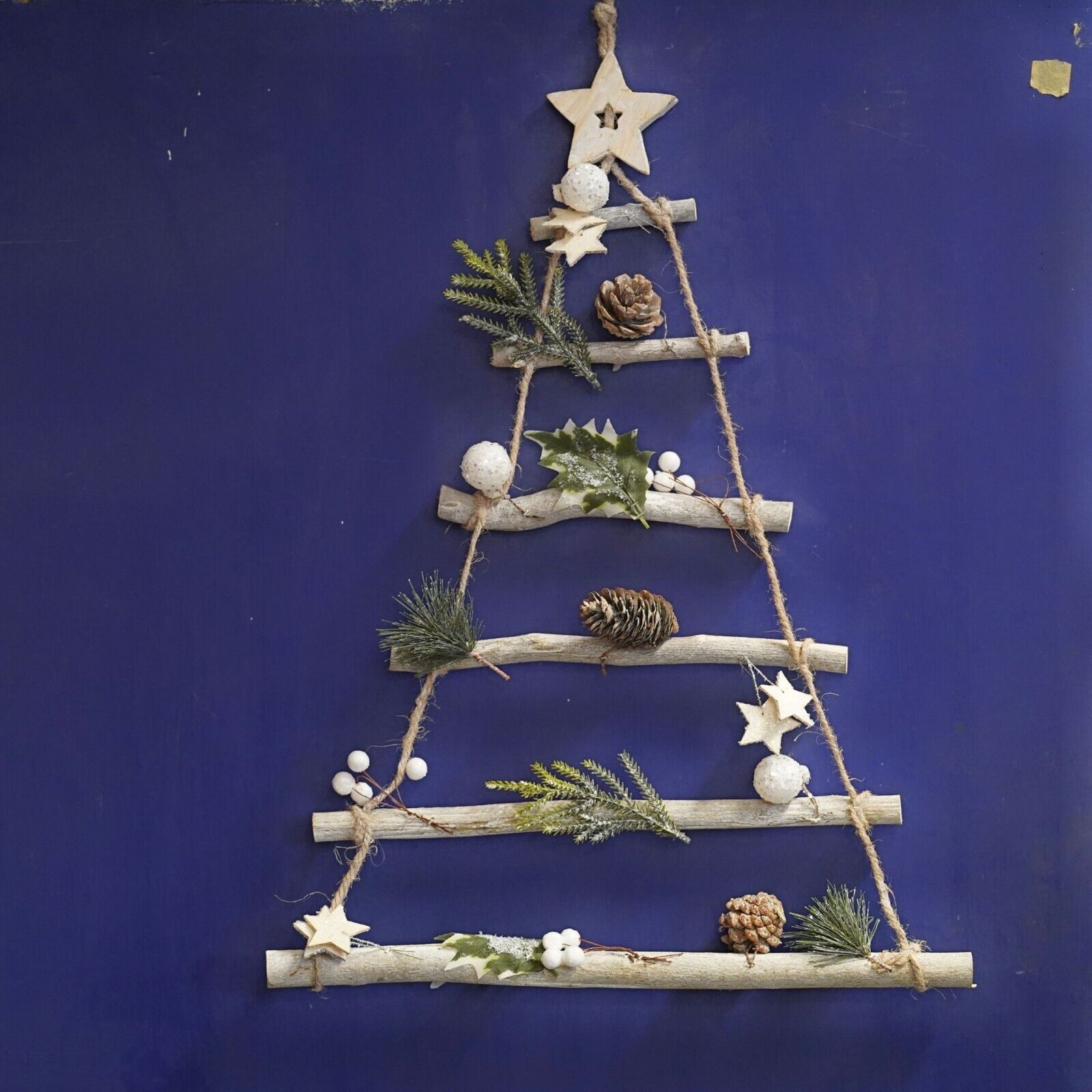 Wooden twigs assembled to resemble a christmas tree, attached with strings and adorned with pinecones and forest leaves with a wooden star on top