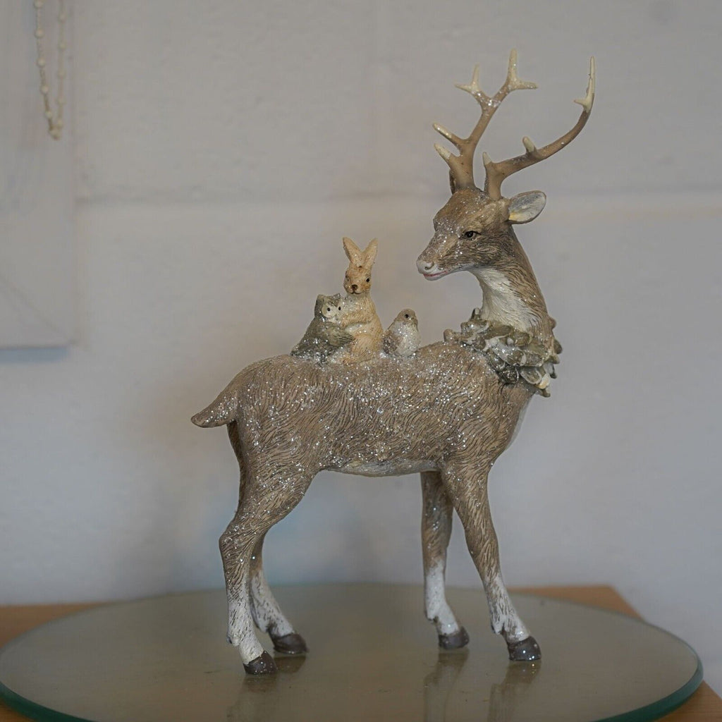 A brown reindeer with forest critters on back. Placed on a glass plinth in a British home with a white wall in background