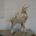 A brown reindeer with forest critters on back. Placed on a glass plinth in a British home with a white wall in background