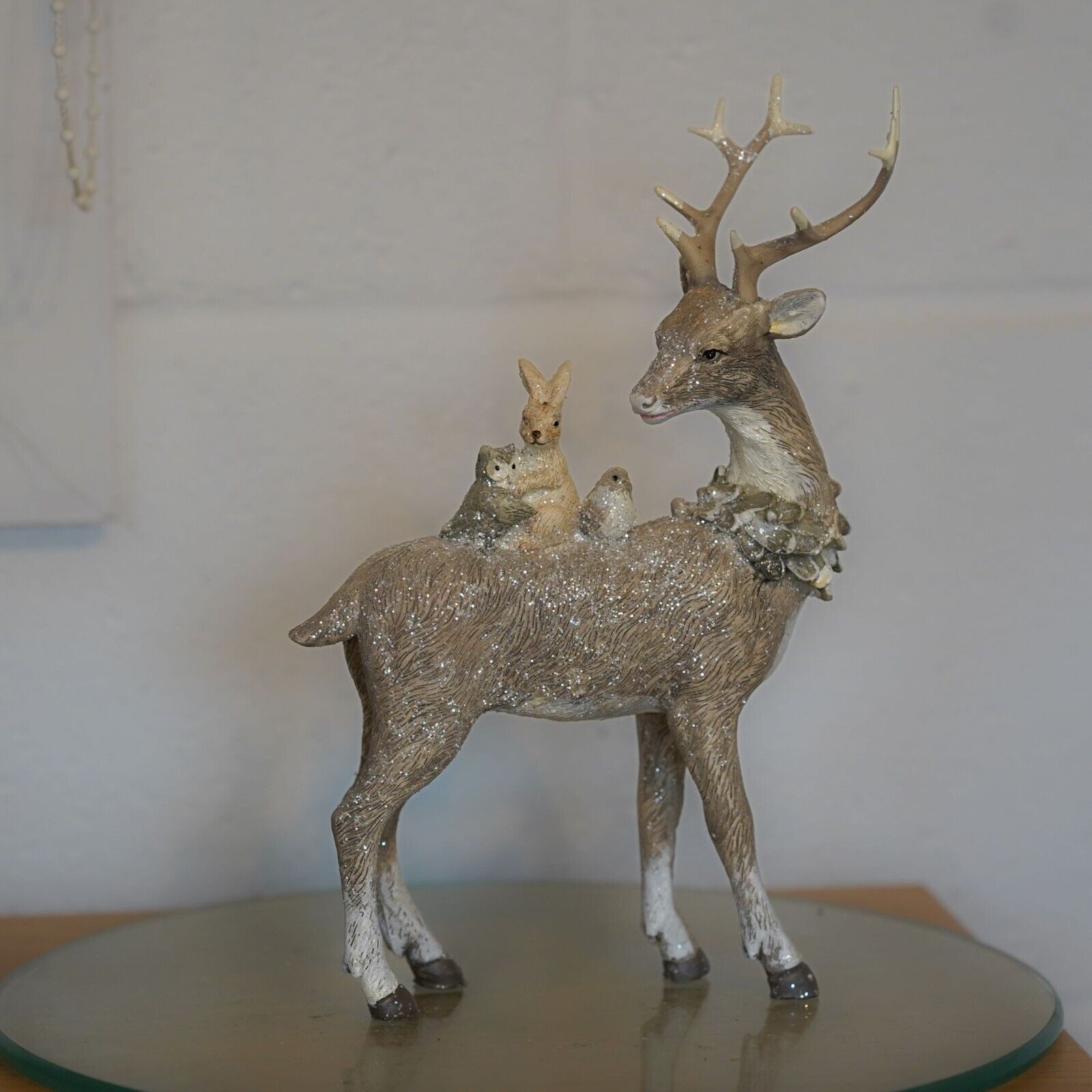 A brown reindeer with forest critters on back. Placed on a glass plinth in a British home with a white wall in background