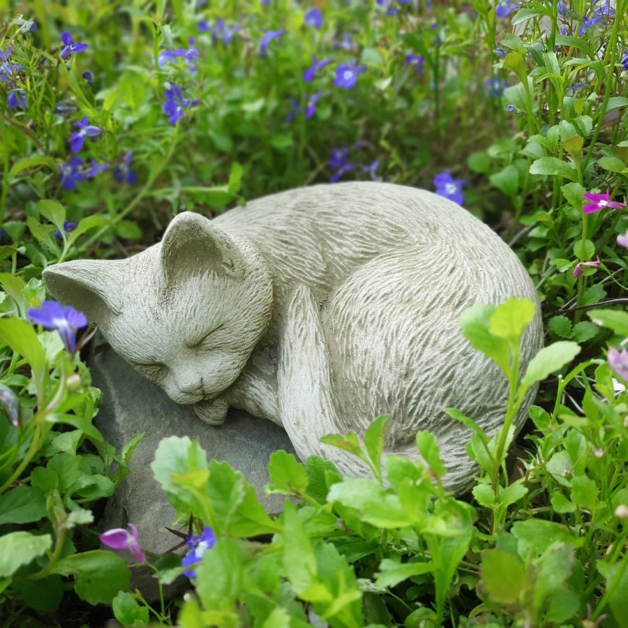 A stone statue of a cat sleeping in a garden.
