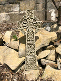 An intricately carved celtic cross situated amongst rocks and stones in a british garden