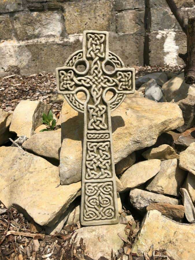 An intricately carved celtic cross situated amongst rocks and stones in a british garden