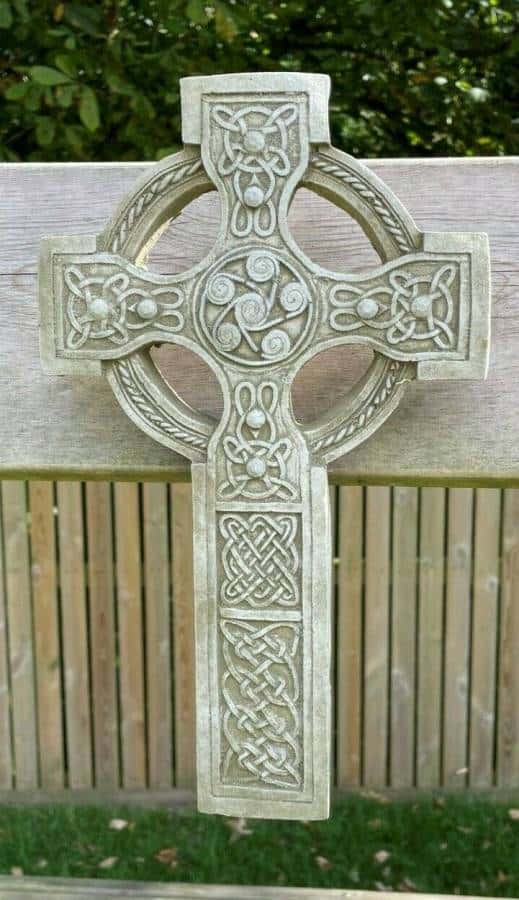 An intricately carved cross featuring celtic 'knots', hanging upon a british garden fence