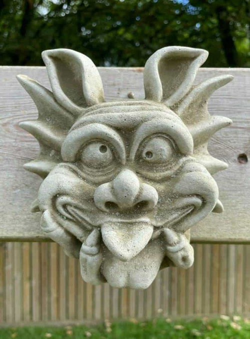 A gremlin face with tongue poked out and eyes crossed cheekily, hanging on a fence in a british garden