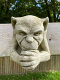 A gargoyle with evil expression and clasped hands, hanging from the wooden fence of a British garden