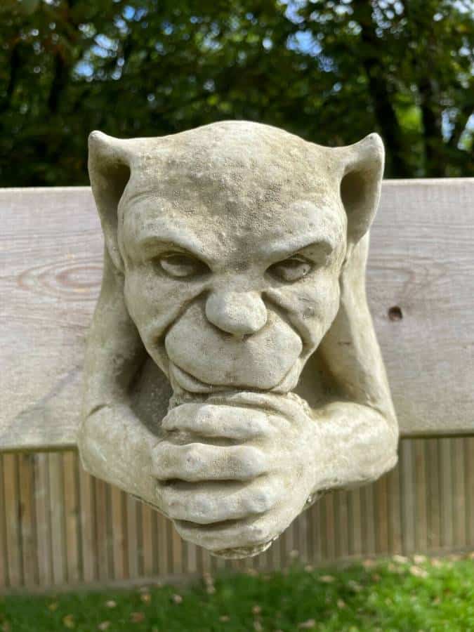 A gargoyle with evil expression and clasped hands, hanging from the wooden fence of a British garden