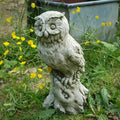 An eagle owl of stone perched on top of a tree stump. Situated amongst the green foliage of a British garden
