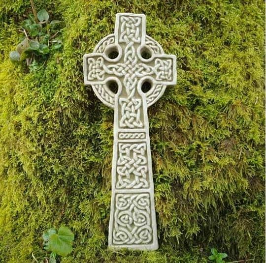 A cross of celtic style with celtic knots decorating from top to bottom. laying in the grass of a british garden