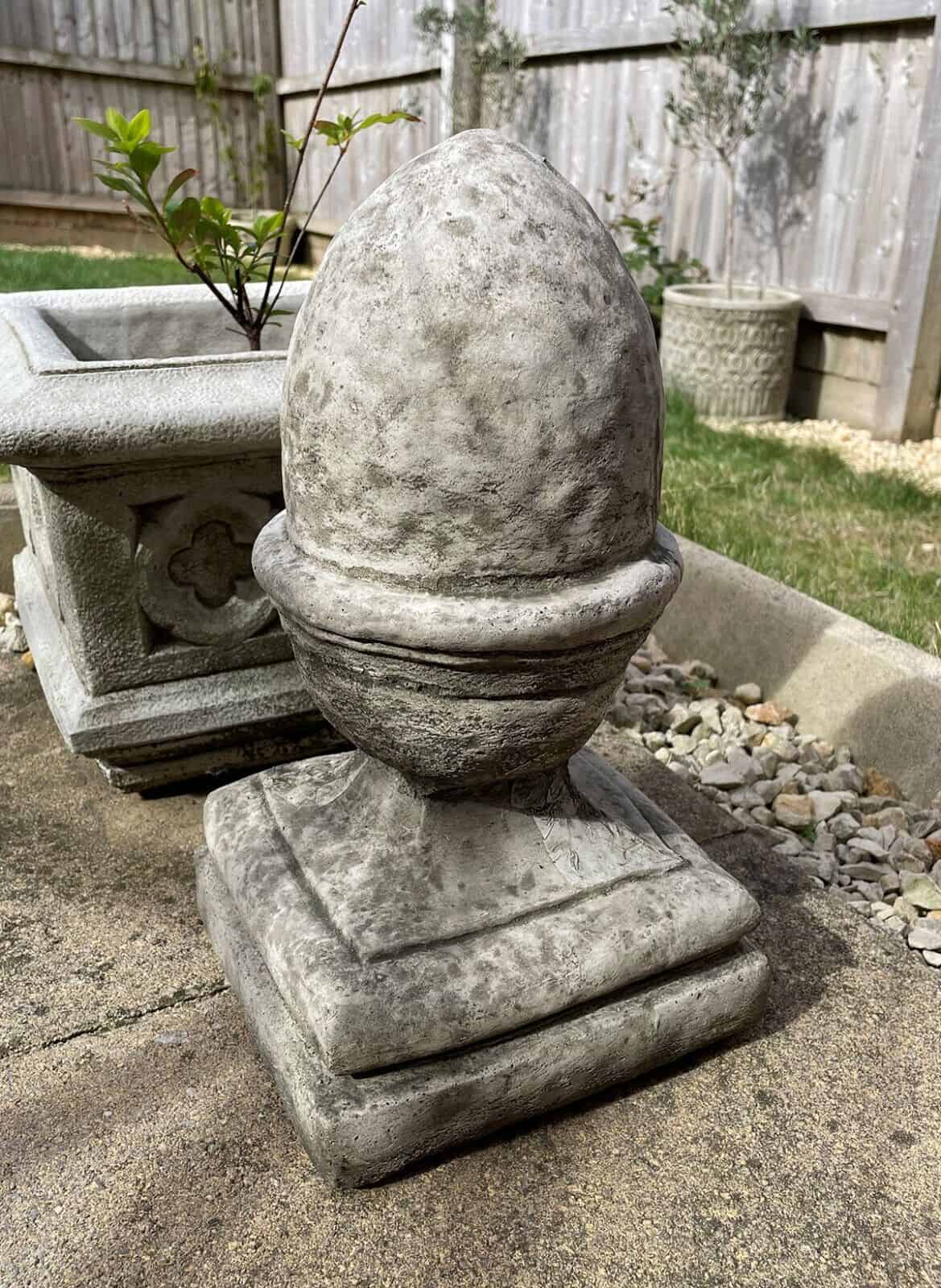 A sizeable finial shaped as an upside-down acorn with a square base. Situated in a British garden