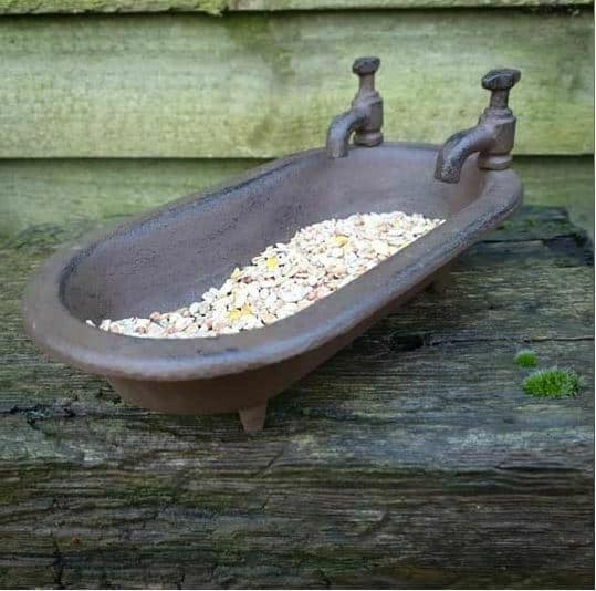 A miniature bathtub with two taps, situated in a british garden and filled with birdfeed