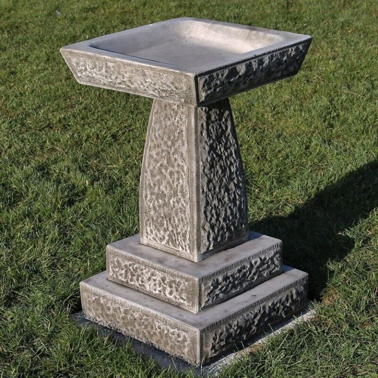 A beautifully unique, squared off bird bath with intricate patterns from base to top. Situated on the grassy garden of a luxury british home