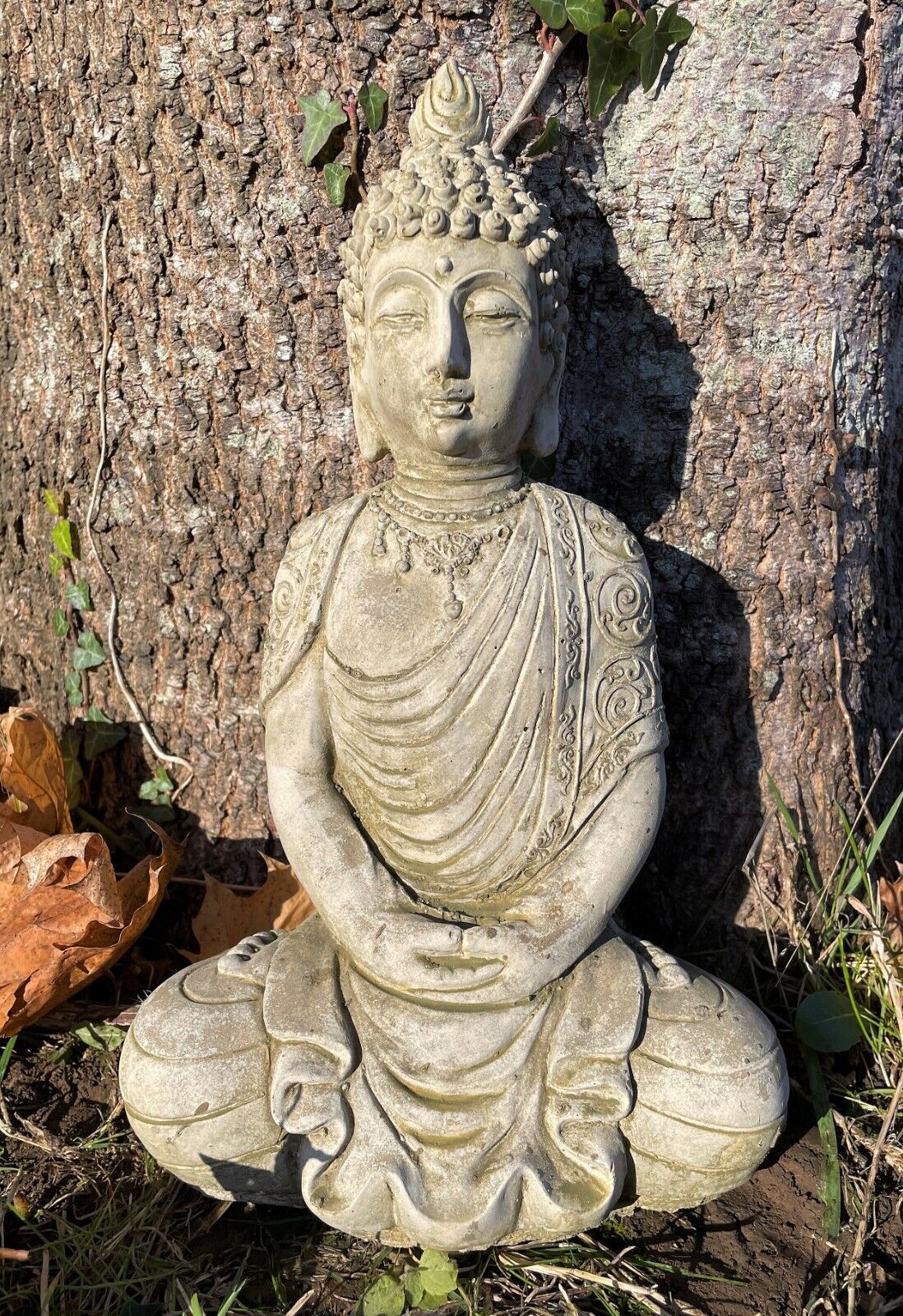 A peaceful buddha with flowing robes in meditation. Situated in a British garden with a tree in background