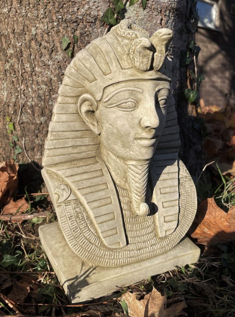 A bust of Pharaoh Tutankhamun wearing their ceremonial hat. Situated in a British garden in front of a tree