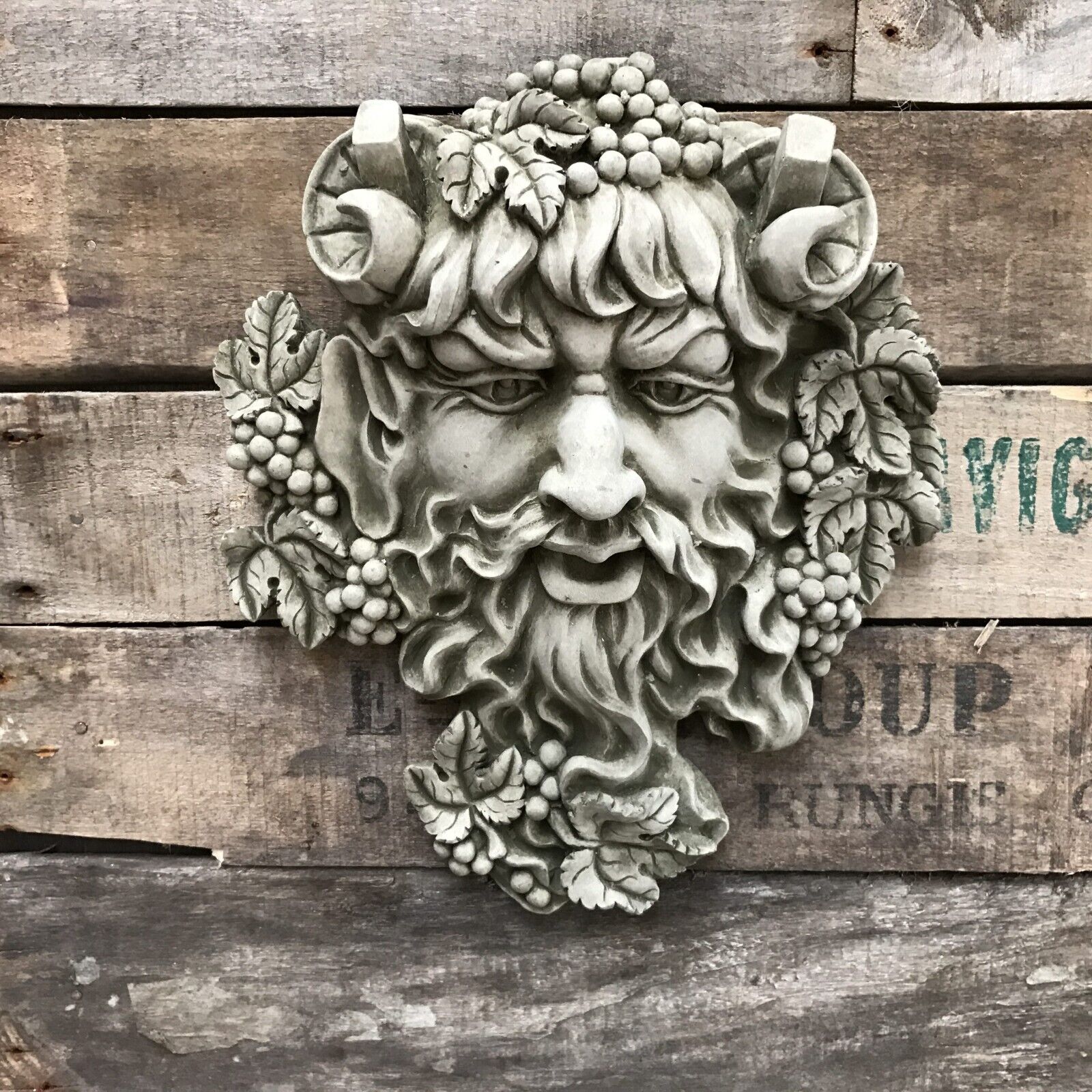 An ancient face with curled horns, large ears and flowing beard intwined with leaves and berries.