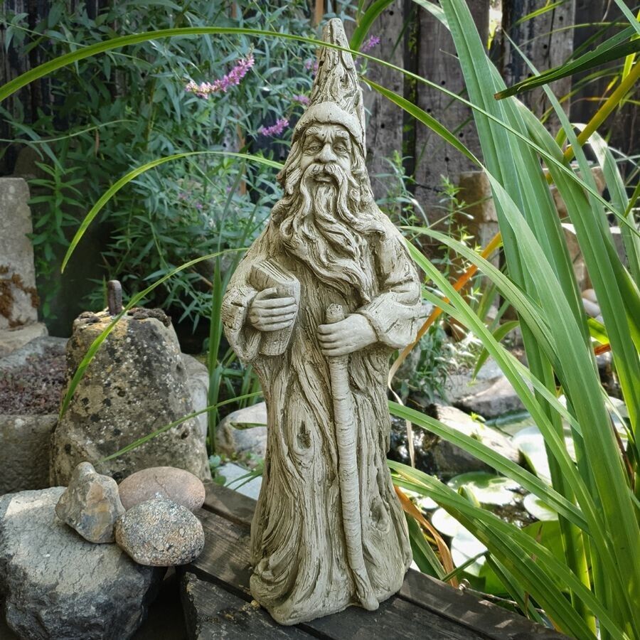 A pointy-hatted, fully robed wizard holding book and staff. Situated amongst the flora of a British garden