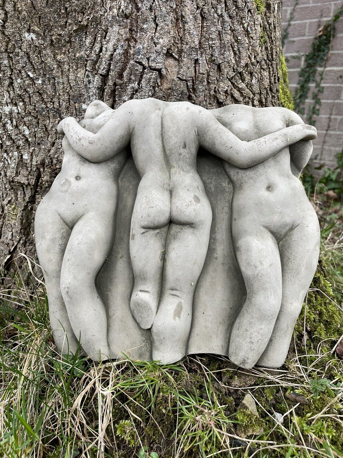 Three naked female figure of ancient Greek design situated amongst the grass of a British garden with tree in background