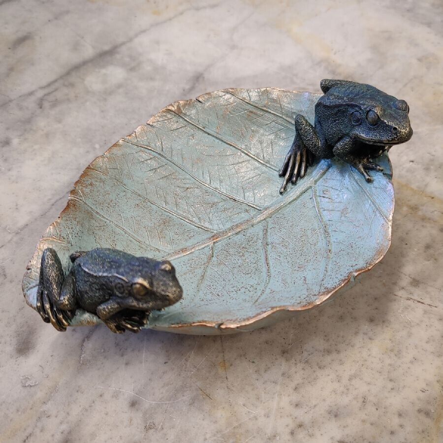 A leaf with flecks of gold with two dark, miniature frogs perched either side. Situated on the marble table of a British home