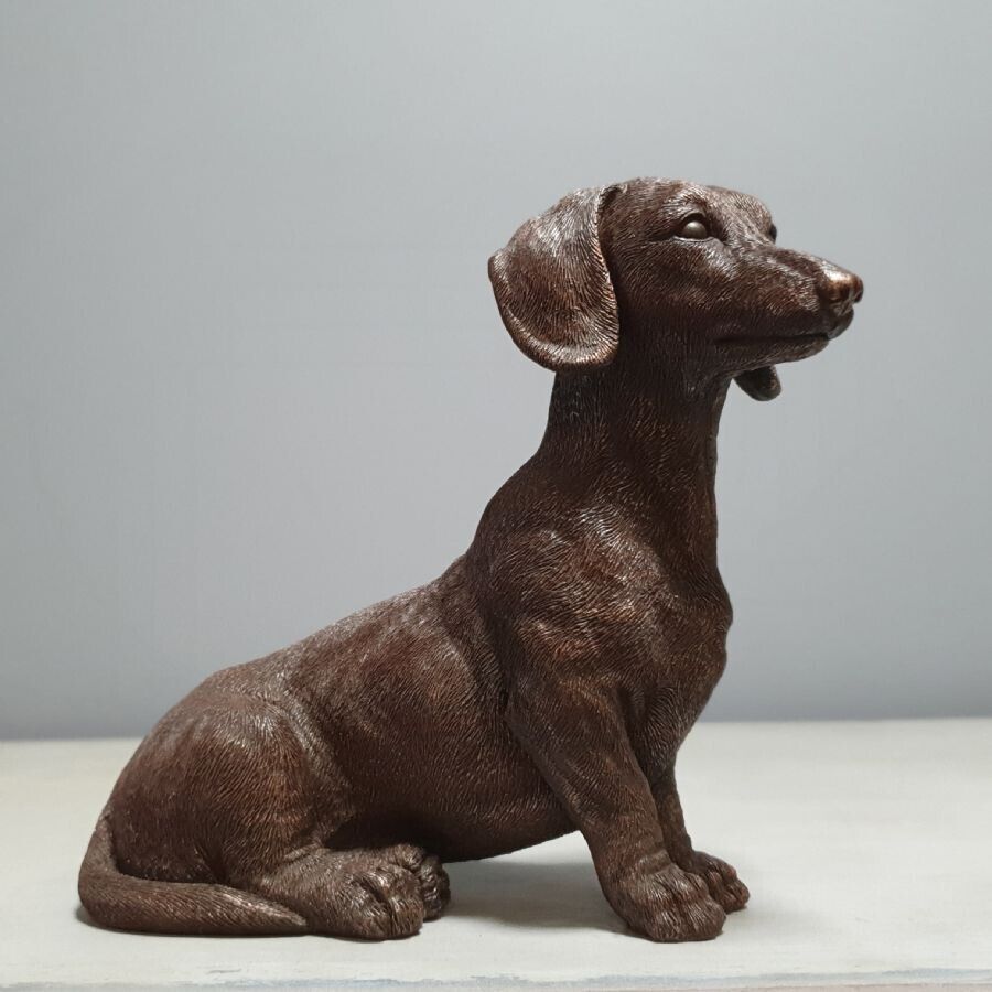 A dachshund puppy dog in bronze finish sitting with an inquisitive expression. Situated on the marble table of a British home