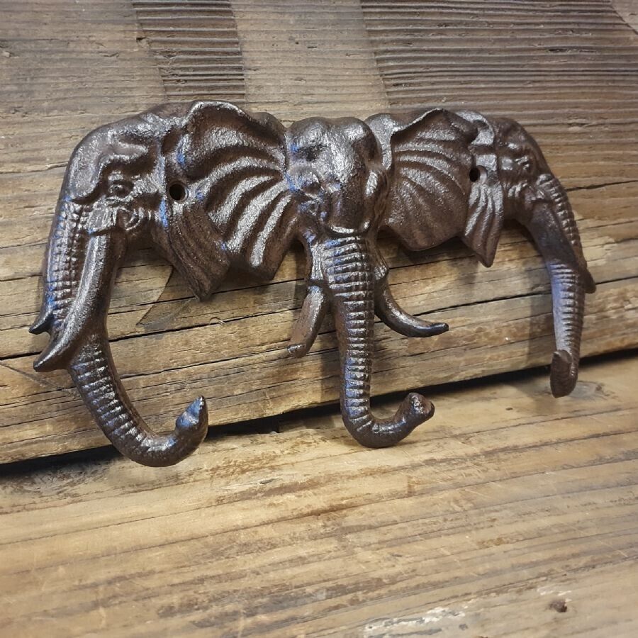 Three elephant heads with trunks extended to form hooks for coats or keys. A cast iron, dark brown finish. Situated on wooden planks in a photography studio